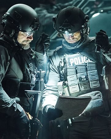 2 men suited up looking at plans